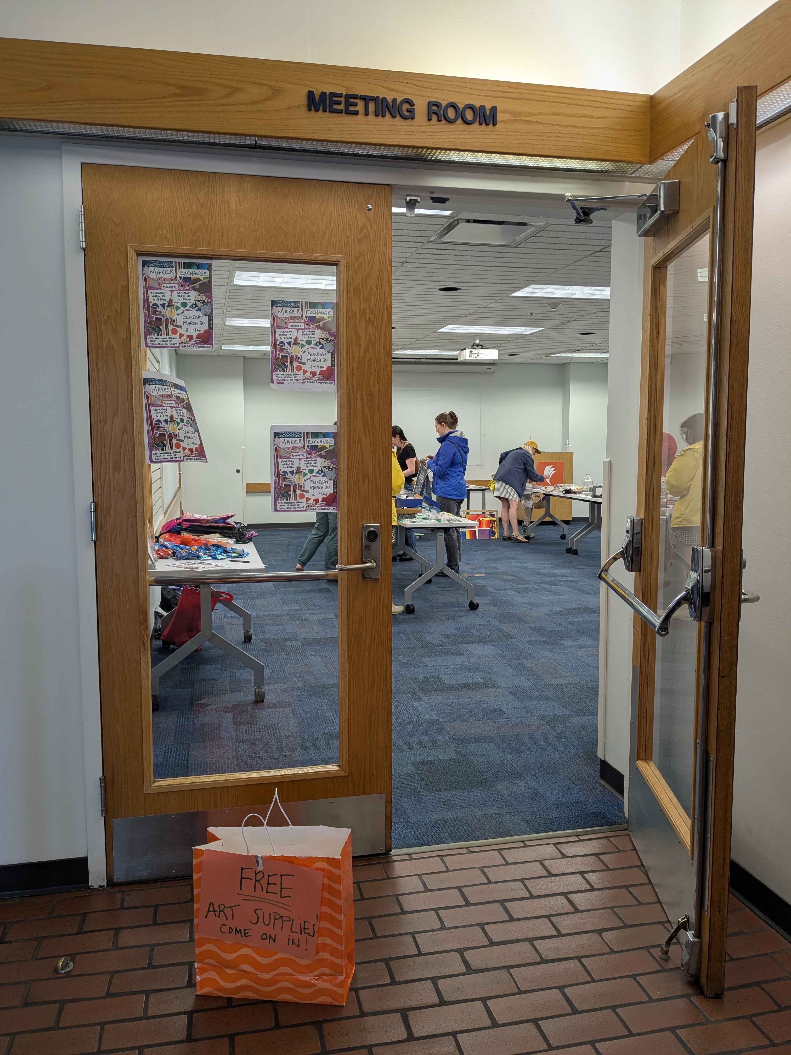 Meeting room doors with sign out front that says Free Come on in and people browsing at tables in the background